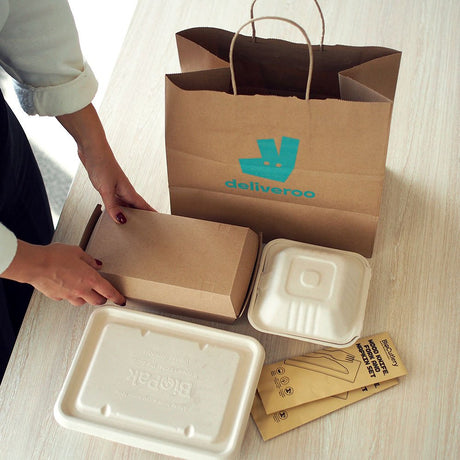 plastic alternative takeout packaging such as kraft paper burger boxes and bagasse containers being put into a kraft paper takeout bag for delivery