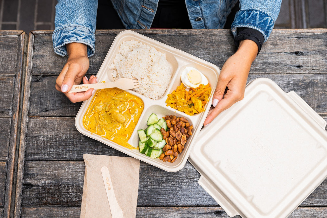 multi compartment takeaway container and compostable lid serving chicken curry and rice with vegetables paired with a wooden cutlery and napkin pack