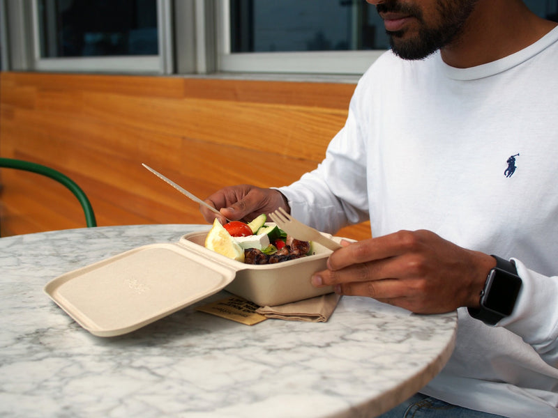 a man eating a feta greek salad from a bagasse clamshell 7 x 5" with wooden cutlery and a kraft napkin