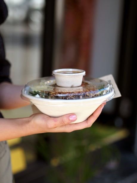 bagasse takeaway bowl and recyclable lid being held by a woman leaving a fast food restaurant