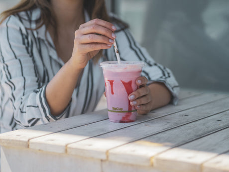 compostable clear cold cup serving a smoothie drank through a paper straw at a sunny cafe