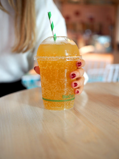 striped green and white paper straw in a compostable pla takeout cup containing juice at a cafe