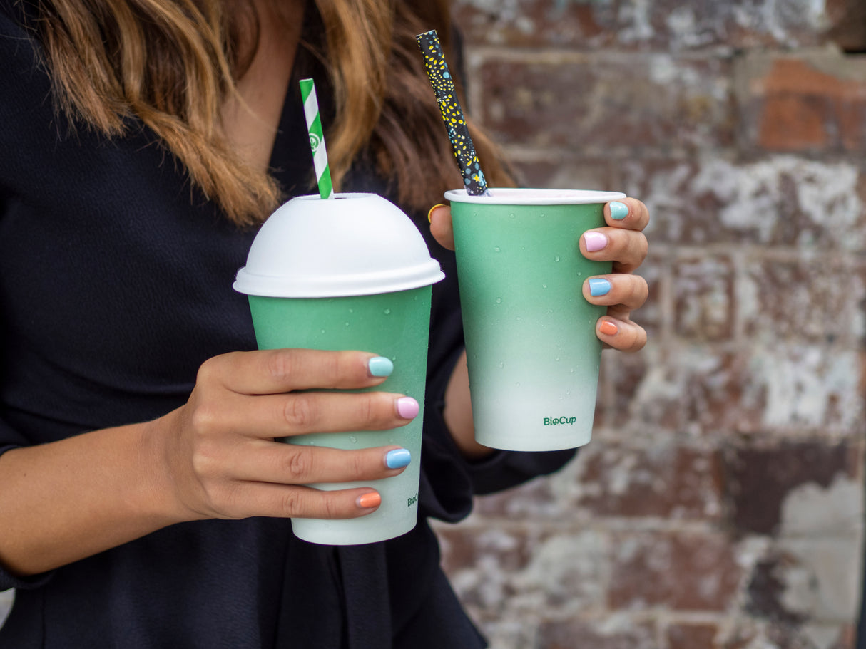 disposable paper cup with bagasse domed lid and paper straw being held by a customer leaving a food establishment