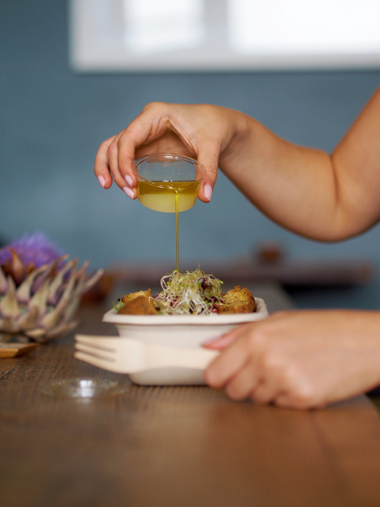 pouring sauce from a pla disposable sauce pot on a takeaway dish served in a rectangular bagasse takeaway container