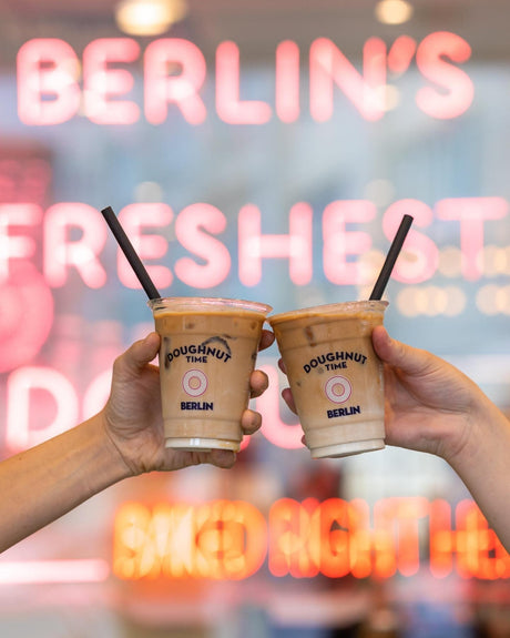 two custom printed plastic cups with paper straws raised in the air celebrating