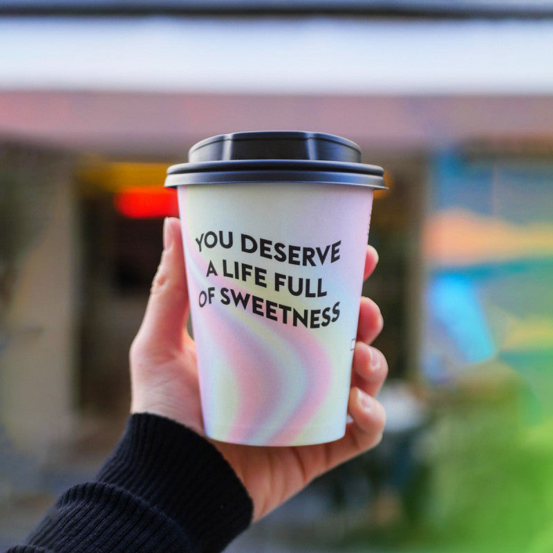 multi coloured custom branded single wall cup and black coffee cup lid in a persons hand