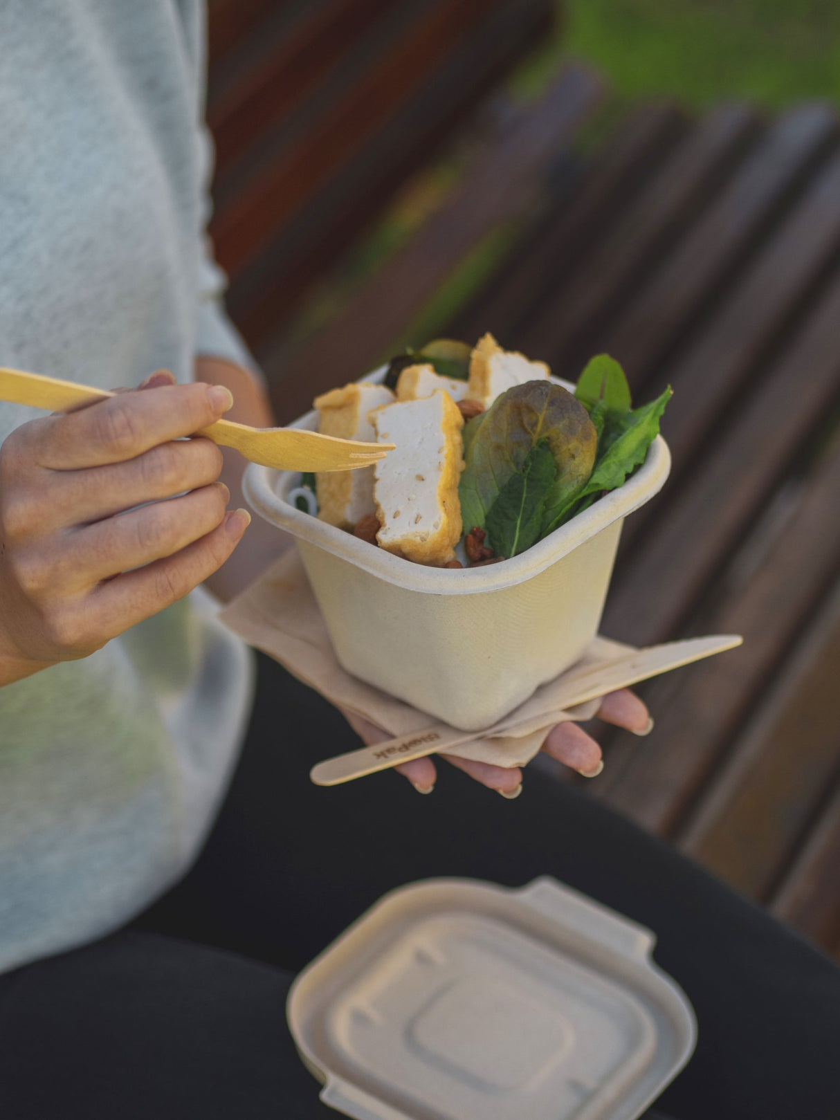 square takeaway container and lid serving tofu with a wooden fork