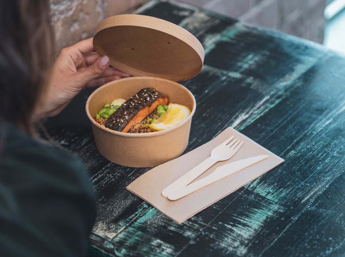 takeaway kraft bowl with kraft lid serving a salmon dish paired with napkins and wooden cutlery