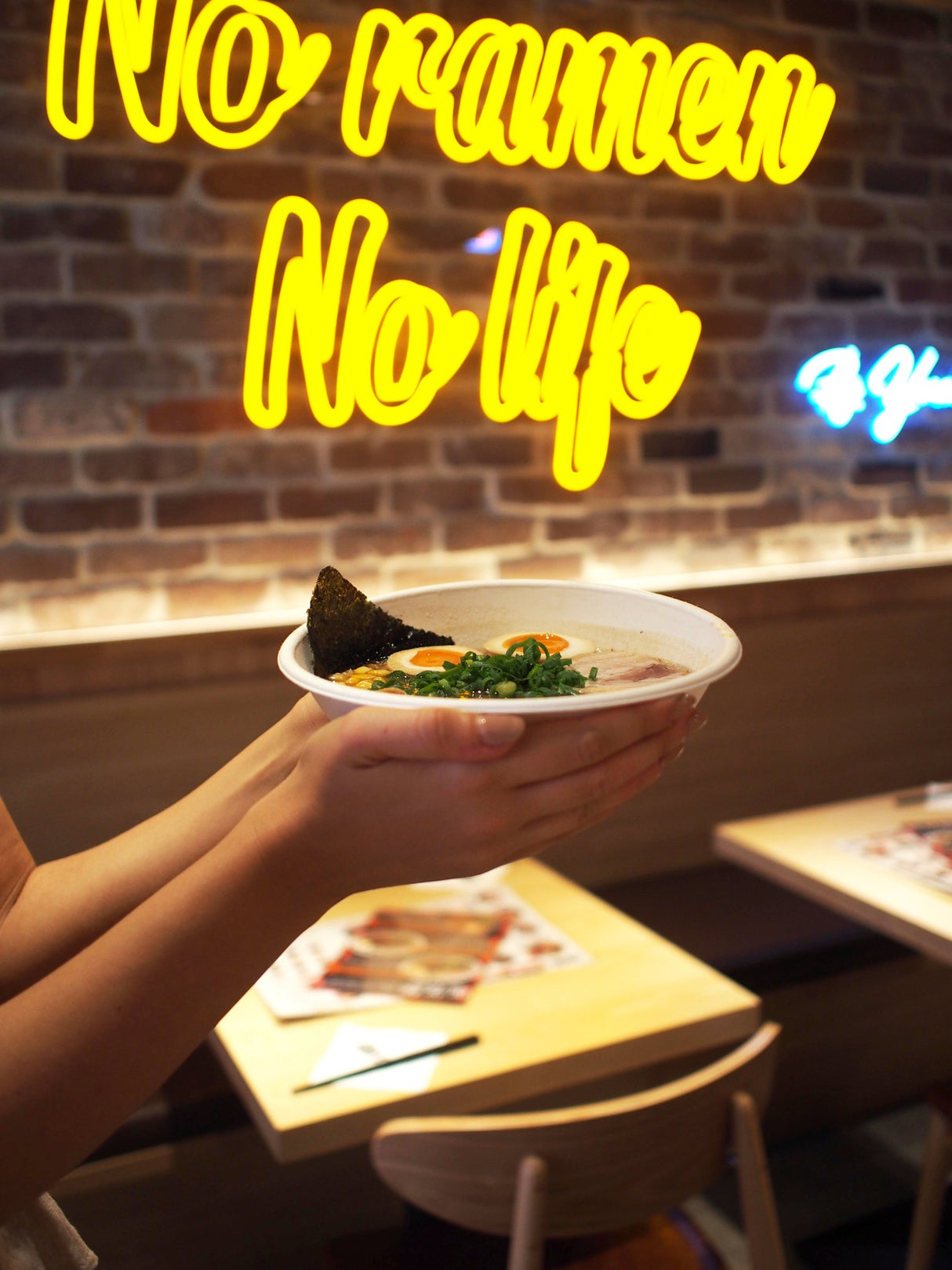 takeout ramen bowl with egg and vegetables being held out right